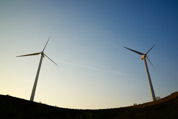 Silhouettes of wind turbines on a hill at sunrise.