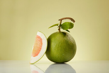 A pink pomelo (Citrus maxima) with a pink pomelo slice leaning on it isolated on minimalist light...