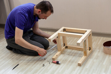 Man with a tape measure measures the detail of the wooden stool