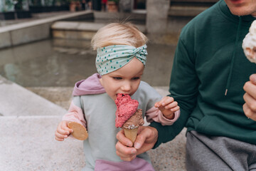 Dad feeds daughter with berry ice cream in a waffle cone, close-up