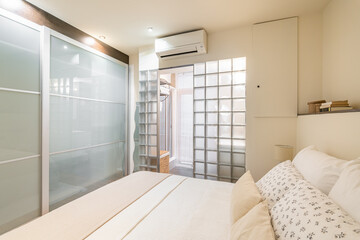 Fototapeta na wymiar Bedroom in modern design with glass blocks and wardrobe with air conditioning and a toilet and a cozy double bed with pillows in white color. Discreet but modern design concept