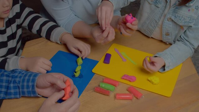 Close-up of multigenerational family molding handicraft toys from colorful playdough, developing creative skills and imagination of kids while enjoying leisure indoors. High angle view.
