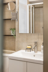 Close-up fragment of stylish bathroom with beige mosaic tiles, mirror, sink and shelves for things. Concept of a comfortable and practical bathroom in a small apartment