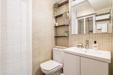 Modern style bathroom with beige mosaic tiles with white sink and toilet and large window for...