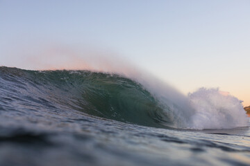 huge powerful wave crashing in the ocean at sunrise