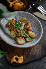 Fried potatoes with chanterelles and green onions in a gray bowl. Vegan dish with potatoes and mushrooms