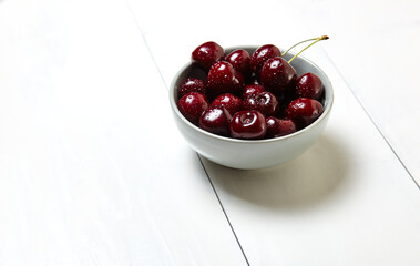 Sweet cherries in a ceramic bowl on wooden background, closeup. Fresh ripe sweet cherries in a bowl with droplets of water