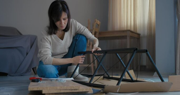 Woman watching furniture assembly instructions while assembling flat pack furniture DIY