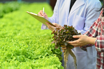Biotechnologist writing on clipboard while working on research at plantation in industrial...