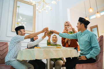 a group of Muslim friends cheers with glasses while breaking their fast at the dining table