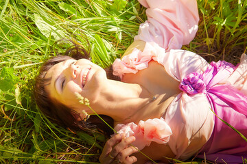 Beautiful girl in a lush pink ball gown in green field during blooming of flowers and blue sky on background. Model posing on nature landscape as princess from fary tale © keleny