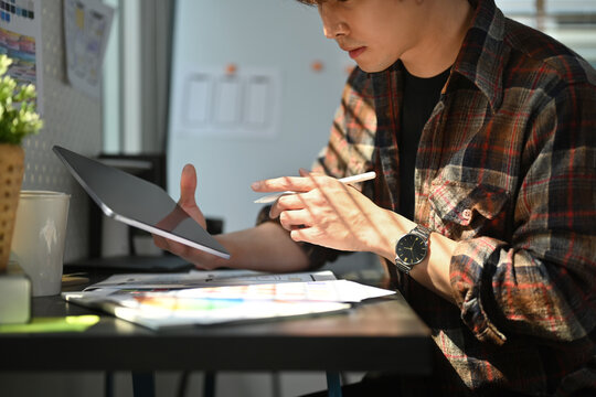 Cropped shot of web developer using digital tablet, working on mobile application software design project at his workstation