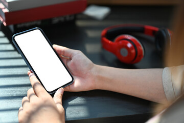 Woman hands holding mobile phone over black wooden working desk. White screen for advertise text or graphic display montage