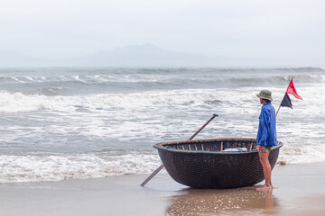 Pêcheur et sa barque traditionnelle en coquille qui attend devant la mer - obrazy, fototapety, plakaty