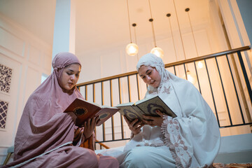 two beautiful Asian girls in hijab recite Quran in prayer room at home