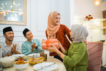 woman in hijab giving a gift to a female friend while gathering at the dining table