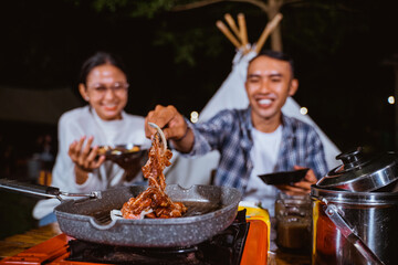 the guy in white t shirt and plaid shirt taking the grilled beef from the grilled pan using the...