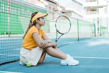 asian female tennis player sitting holding racket on tennis court against net background