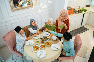 Top view of a group of Muslims cheers with glasses while breaking fast at the dining table
