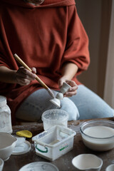 Fototapeta na wymiar Female ceramicist or potter holding paintbrush applying glaze on ceramic pieces while sitting at work table in studio, cropped photo. Production of handmade tableware. Pottery therapy in mental health