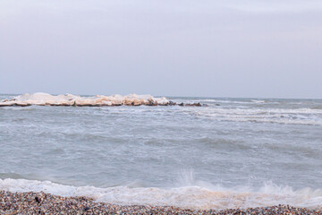 Close-up of the icy seashore, frozen waves, rocks and sun glare on the ice