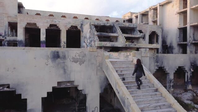 Drone shot view of a girl doing up on stairs of abandoned Jerma Palace Hotel in Malta