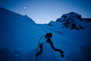 An HD camera sits on a tripod supportted by a block of snow, set up to capture a time-lapse of the night sky.