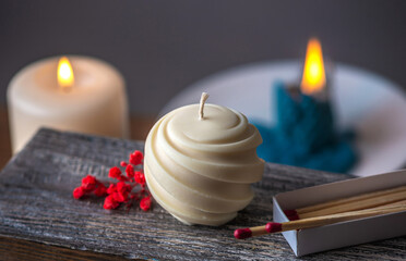 Round carved handmade candle and matches and red flowers on a wooden stand against the background...