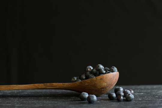 A side view of blueberries in a wooden spoon with a dark background.
