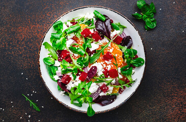 Beet, cheese and orange healthy salad with arugula, lamb lettuce, red onion, walnut and tangerine, brown kitchen table. Fresh useful dish for healthy eating