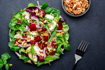 Beet and pear healthy salad with arugula, lamb lettuce, red onion, chard and walnut, black kitchen table. Fresh delicious vegan dish for healthy eating
