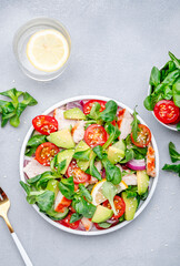 Chicken salad with red tomato,  avocado, cucumber, red onion, lamb lettuce and sesame seeds on gray table background, top view