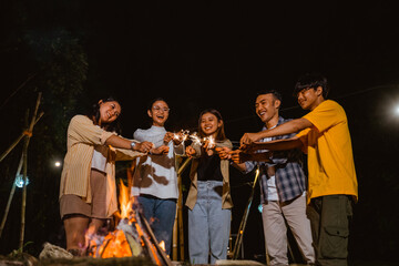 a group of people playing fireworks happily and put its together while standing around the bonfire at the camp site