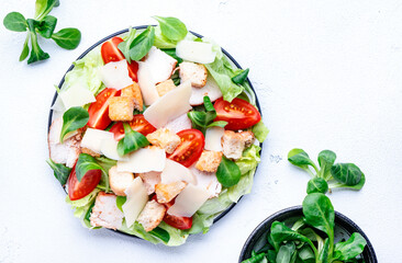 Caesar salad with chicken, iceberg salad, croutons, parmesan cheese and tomatoes with caesar dressing. White table background, top view