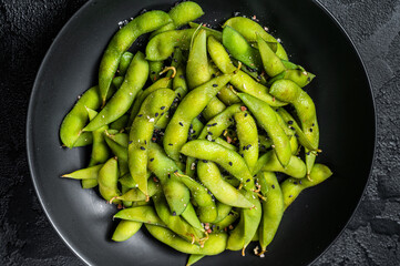 Boiled Edamame Soy Beans with sea salt in a plate. Black background. Top view