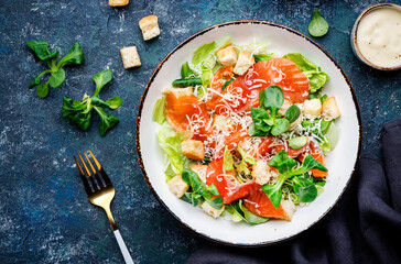 Caesar salad with salted salmon, iceberg and lamb lettuce, croutons, parmesan cheese with caesar dressing. Blue stone table background, top view