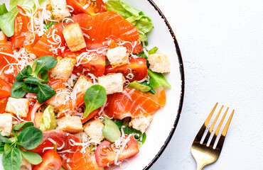 Caesar salad with salted salmon, iceberg and lamb lettuce, croutons, parmesan cheese with caesar dressing. White table background, top view