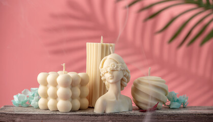 Beautiful white handmade candles of different shapes and sizes on a pink background