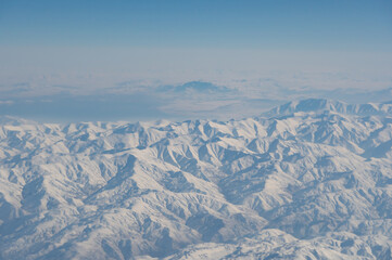 Obraz premium Wing of aerial view of an airplane jet flying above clouds from the window in traveling and transportation concept. White snow mountain in winter season. Nature landscape background.