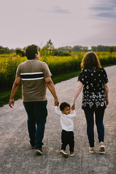 Multiracial family walks along path in grass and flower field