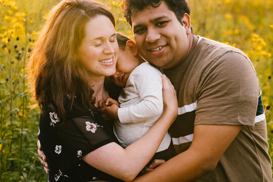 Mom and Dad hug toddler happily in flower field in golden light