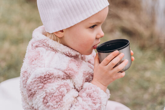 Baby girl drinking tea from a thermos near the river in late autumn