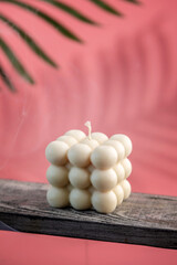 Beautiful handmade candle of interesting shape on a wooden stand and pink background
