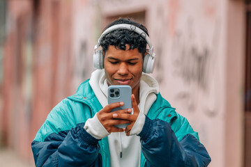 young urban latino man with mobile phone and headphones in the street