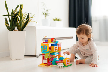 Baby girl playing indoors sitting on floor in playroom at home with constructor. Educational game...