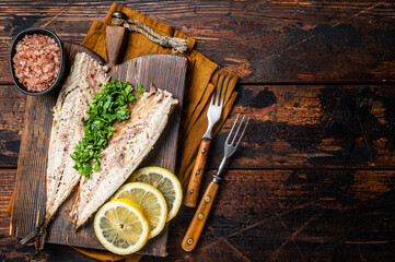 Delicious baked mackerel fillets with greens, garlic and lemon on wooden board. Wooden background....