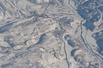 Fototapeta premium Wing of aerial view of an airplane jet flying above clouds from the window in traveling and transportation concept. White snow mountain in winter season. Nature landscape background.