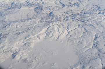 Wing of aerial view of an airplane jet flying above clouds from the window in traveling and transportation concept. White snow mountain in winter season. Nature landscape background.