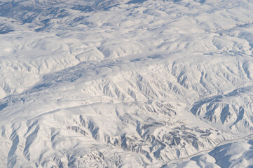 Wing of aerial view of an airplane jet flying above clouds from the window in traveling and transportation concept. White snow mountain in winter season. Nature landscape background.