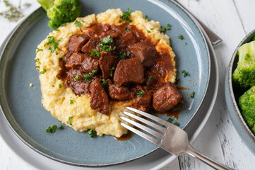 Goulash or ragout with brown sauce and polenta on a plate